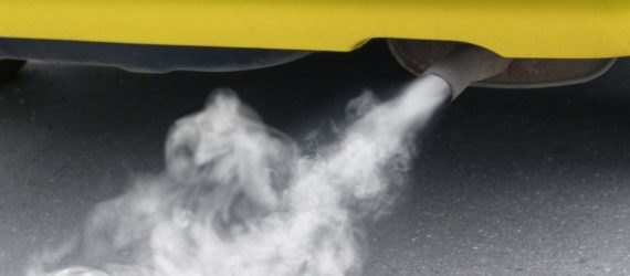 Exhaust, polluting the environment, pours out of a yellow car