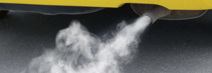 Exhaust, polluting the environment, pours out of a yellow car