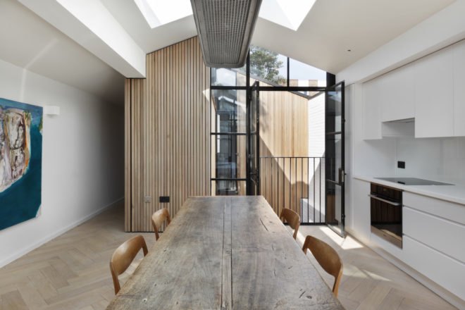 Dining table in center of room with white cabinetry kitchen on one side and wall art on the opposite side