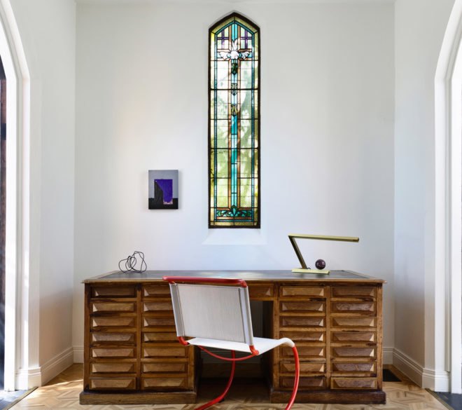 A modern desk and chair underneath a stained glass window.