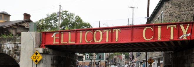 Cars passing under red bridge that reads Ellicott City