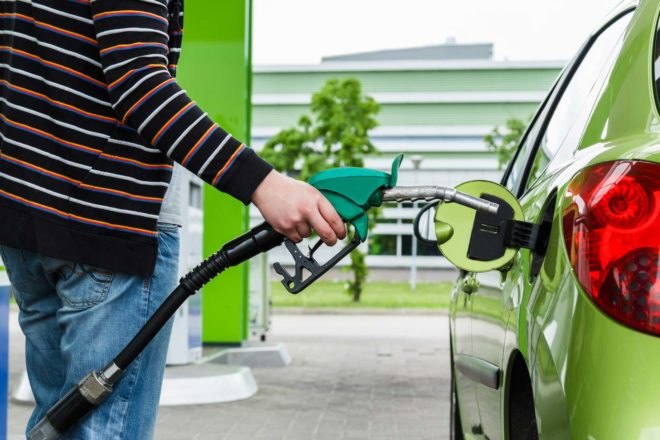 A man using a green gas pump to fill up a green car