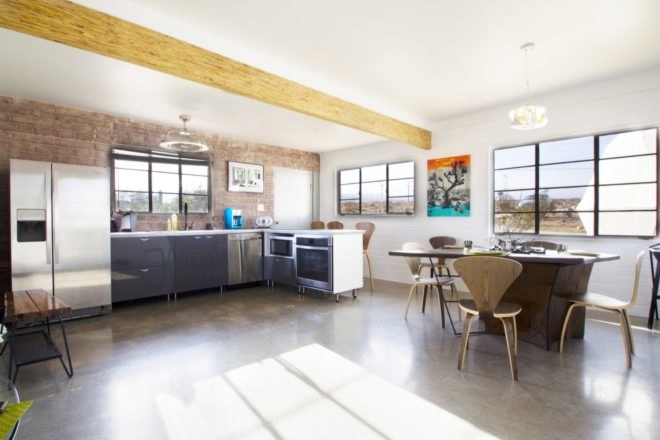 Kitchen has exposed brick wall, dining table, and wooden beam on the ceiling