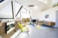 Living room has large windows, brown leather couch, and brightly colored rug and chair