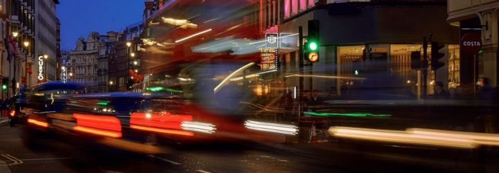 Buses and cars zoom along a busy street in London