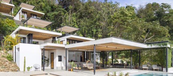 A hotel with white facades in front of a tropical forest.