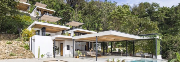 A hotel with white facades in front of a tropical forest.