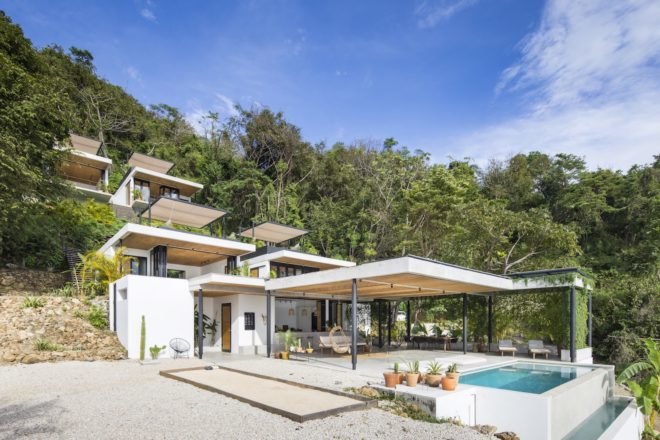 A hotel with white facades in front of a tropical forest.