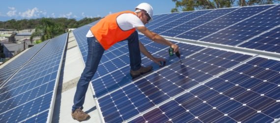 A technician installs solar panels atop a factory roof
