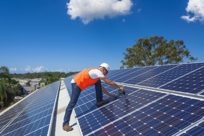 A technician installs solar panels atop a factory roof
