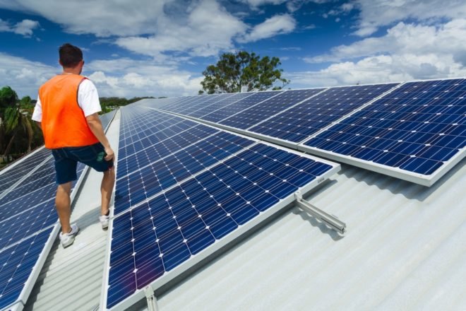 A technician inspects solar panels atop a factory roof