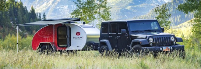 A jeep with a teardrop trailer attached against a backdrop of mountains.