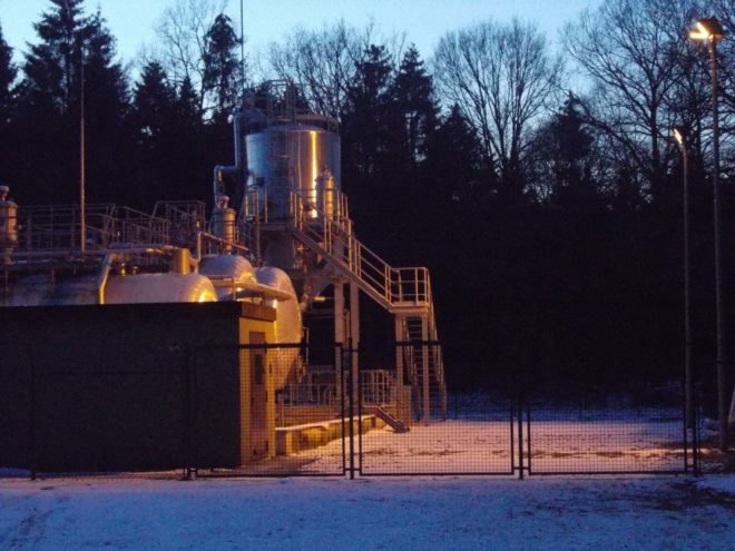 A fracking disposal well in a snowy field with shadowy trees in the background