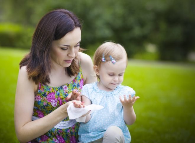 A mother cleans her daughter's hand with a wet wipe in a park