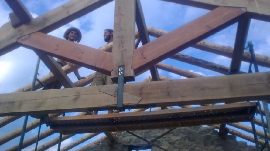 Two men on top of the frame of a roof