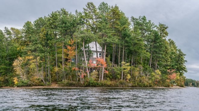 view of a lake house through trees with water in foreground