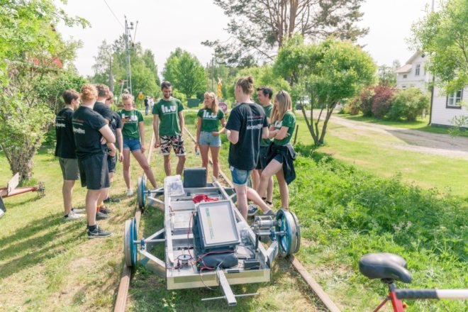 Biodegradable vehicle on tracks with students in background