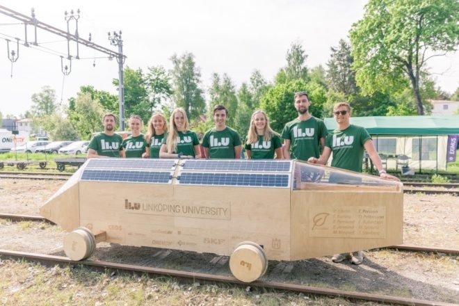 Biodegradable vehicle on tracks with students in background