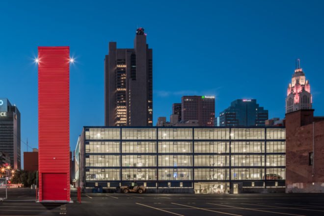 tall red shipping container tower in front of a building