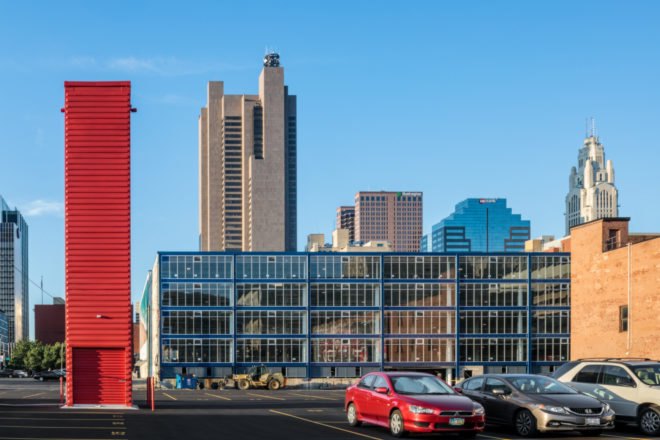 tall red shipping container tower in front of a building