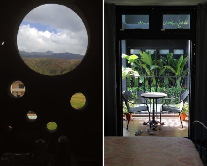 On the left, large round window with view of mountains in the background. On the right, small balcony with chairs and a table.