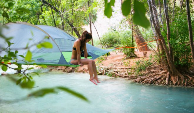 Woman camping in tent in the trees above a river.