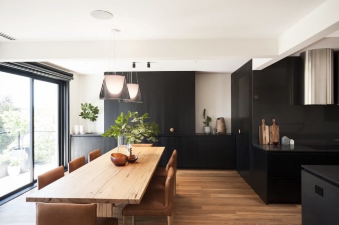 long, light-wood dining table and tan leather chairs under dark pendant lights