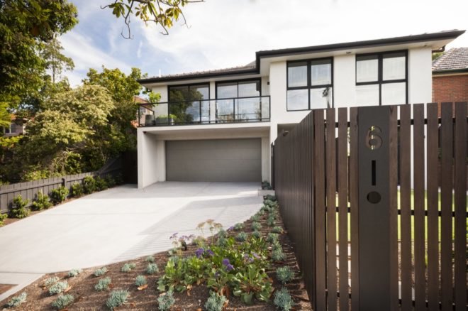 Driveway lined with plants leading up to multi-story home with dark wood fencing