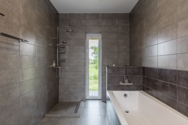 bathroom with large bathtub, shower head, and gray tiling