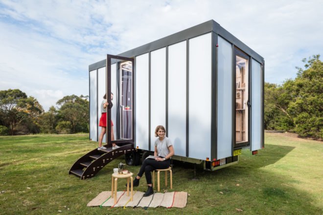 white tiny home with person sitting outside in a chair