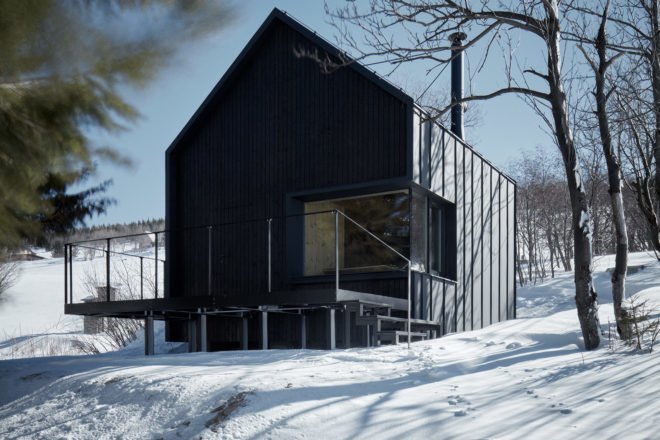Black cabin with gabled roof and large deck