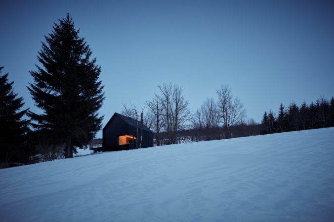 Black cabin on snowy hill at dusk