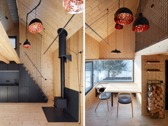 On the left, black timber kitchen and a dark wood burning stove. On the right, pendant lights hang above a small dining table