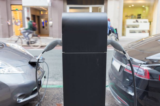 Two electric cars parked along a street and charging