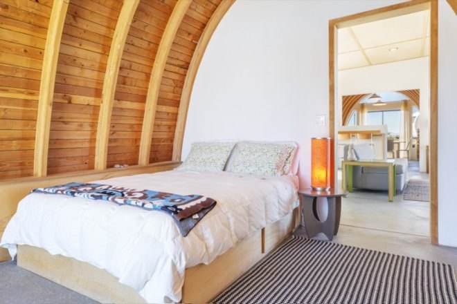 bed with white bedding and a small night stand with an orange lamp under a curved wood ceiling