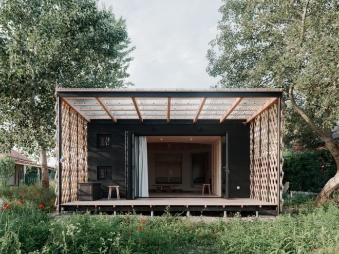 dark cabin with wooden terrace, large doors opened to the inside, and timber lattice on each side of the terrace