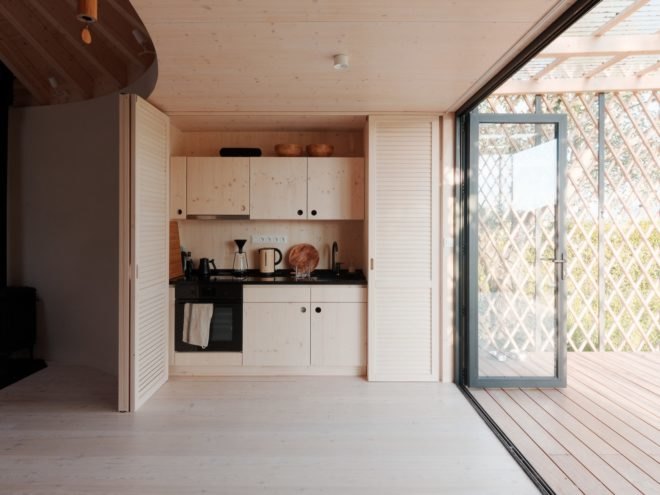 kitchen area with light timber cabinets behind folding light timber doors