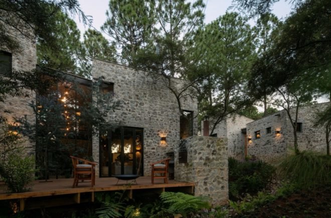 Stone home with large glass windows and a wood patios with chairs