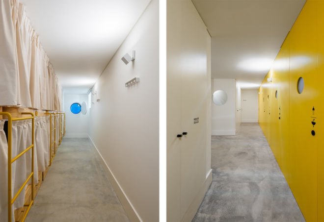 On the left, yellow bunk-beds in a row with white privacy curtains. On the right, line of bathrooms with yellow doors on a yellow wall