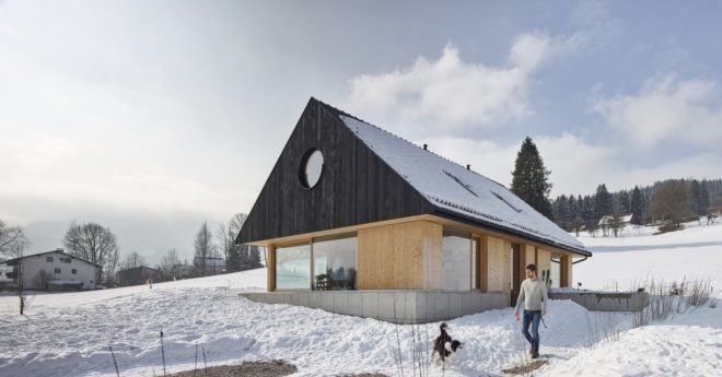 Man playing with dog outside of light timber home with dark gabled roof