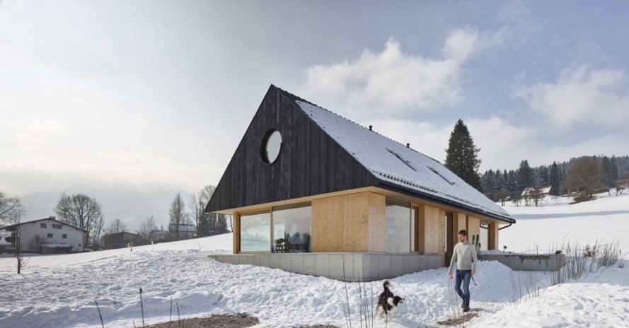 Man playing with dog outside of light timber home with dark gabled roof