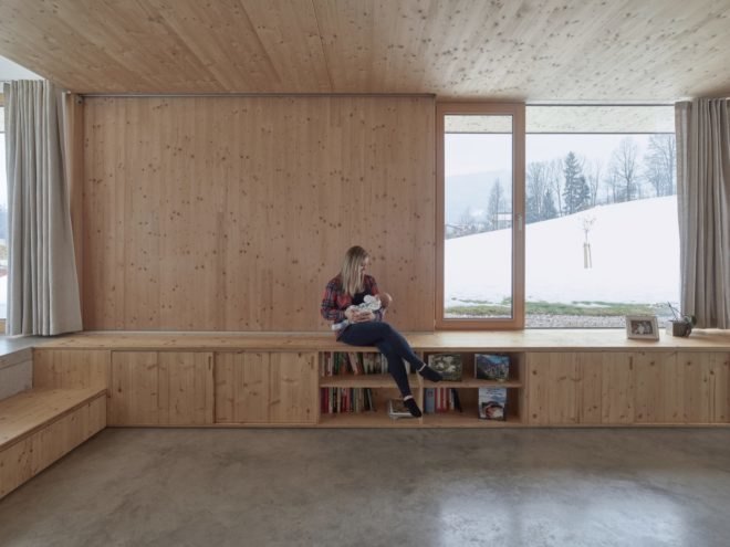 Mother holding a baby sitting on wooden bench and bookcase in living room