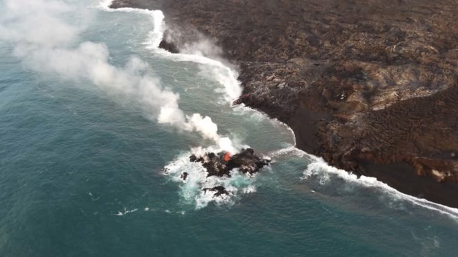 zoomed out view of new volcanic island in ocean with smoke rising in air