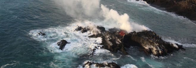 new volcanic island in ocean with smoke rising in air