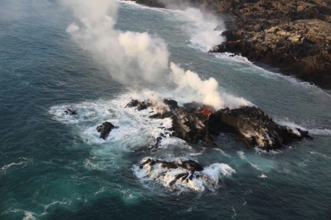 new volcanic island in ocean with smoke rising in air