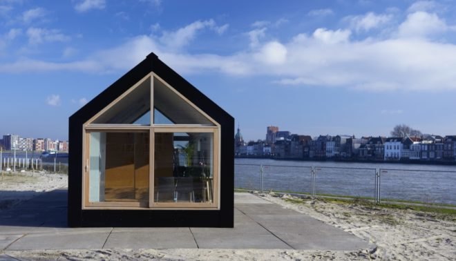 exterior of black tiny house with water in background