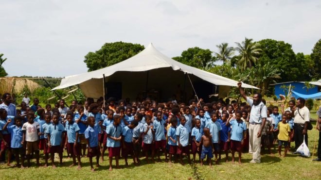 children and adults standing outside a constructed school in a box