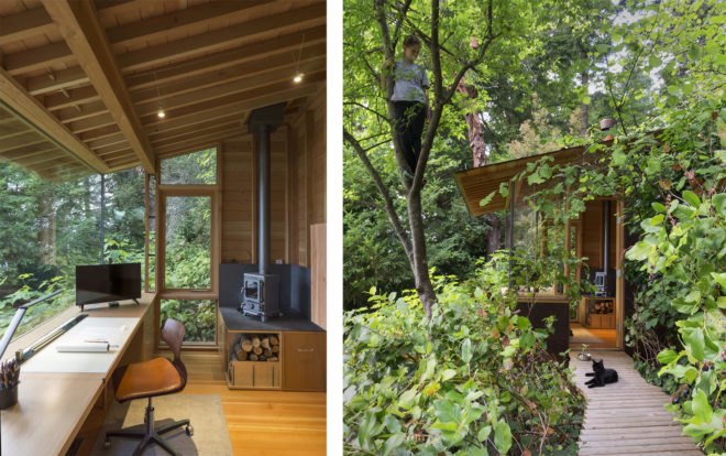 On the left, long desk against glass wall and small wood-burning stove in the corner. On the right, child climbing in a tree outside the cabin.
