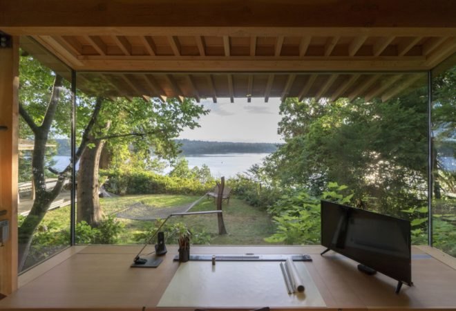 Desk and architect tools in front of a large window with views of water and trees