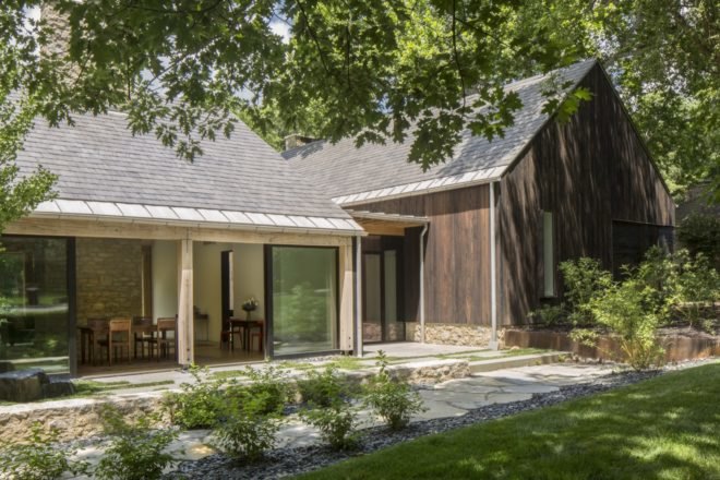 wood farmhouse with large sliding glass doors and stone walkway